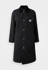 Manteau noir long avec boutons-pression, col en velours côtelé, poche poitrine zippée et deux poches latérales, vue de face sur fond blanc.