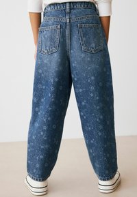 Jeans in denim di colore blu scuro con un motivo di stelle e lune, dotati di vita alta, vestibilità ampia e cinque tasche. Accentuati da cuciture in contrasto.