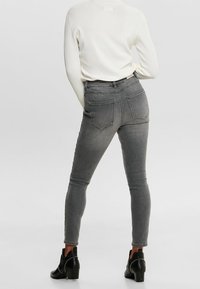 Jeans gris ajustados con cintura alta y diseño de cinco bolsillos, combinados con un suéter blanco de canalé y botines negros de tacón.