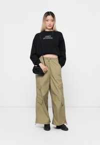 Mustmustelane cropped-sweater, millel on tekst "OBEY STUDIOS", koos heledate roheliste cargo-pükstega, millel on taskud, elastne vöökoht ja reguleeritavad pahkluud.