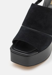 Sandale plateforme en daim noir avec large bride et bout carré ouvert sur fond blanc.