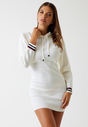 Abito felpa bianco con maniche lunghe, dettagli a costine in bordeaux, verde e nero. Presenta un cappuccio con coulisse e una silhouette aderente.