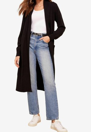 Lang sort cardigan lavet af blødt strik, parret med lys blå jeans med høj talje og hvide sneakers. Casual design med løs pasform og lommer.