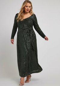 Vestido largo de lentejuelas verdes con mangas largas, escote en V y un detalle de lazo en la cintura, que presenta una silueta fluida y una textura brillante.