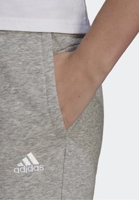 Grijze trainingsbroek met een gestructureerd uiterlijk, voorzien van zijzakken en een geborduurd wit Adidas-logo op de linker heup.