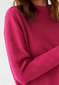 Fuchsia Pullover mit einer sanften Textur, verfügt über einen hohen Kragen und lange Ärmel, zeigt eine legere Passform ohne sichtbare Verschlüsse oder Muster.