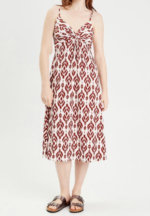 Femme portant une robe sans manches, longueur au genou, avec un motif géométrique rouge et blanc et des sandales à boucle métallique.