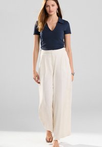Marineblå kortærmet v-hals top parret med løstsiddende, høj talje cremefarvede bukser. Modellen bærer strappy sandaler og et sølvarmbånd.