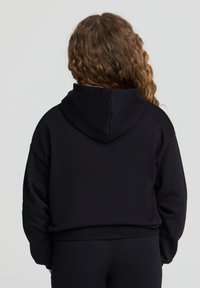 Felpa nera con cappuccio, dalla vestibilità rilassata, con polsini e orlo a costine. Tessuto testurizzato, cuciture visibili e un piccolo logo sulla parte posteriore.