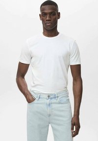 Tricou alb din bumbac cu guler rotund, mâneci scurte, asortat cu jeansi din denim albastru deschis cu închidere cu nasture și o ușoară decolorare.