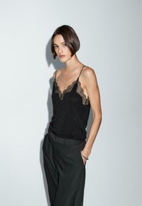 Camisole noire avec bordure en dentelle, dotée de fines bretelles réglables et d'une coupe décontractée, associée à un pantalon sombre taille haute.