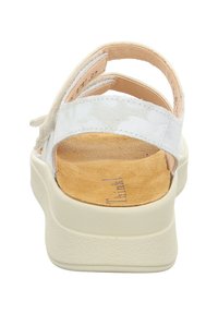 Witte sandaal met een gestructureerde bovenkant, verstelbare achterkant en gevoerd bruin voetbed. Voorzien van een dikke, crème-kleurige rubberen zool.