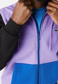 Felpa con zip viola e nera con un accento blu in fondo, realizzata in tessuto testurizzato e con un piccolo logo sul petto.