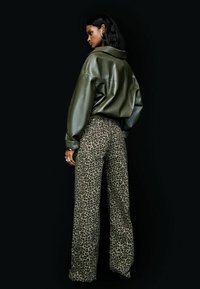 Overgemaakte olijfgroene faux leren jas gecombineerd met losse leopardprint broeken met hoge taille en zilveren studs.