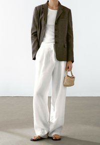 Ruskea bleiseri nappien kanssa, valkoinen toppi, leikkauksettomat valkoiset pellavahousut, mustat litteät sandaalit ja pieni kudottu käsilaukku. Sujuvat tekstuurit läpi kokonaisuuden.