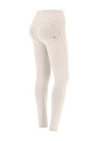 Leggings beige con una texture liscia, vita alta e tasche posteriori curve. Presentano cuciture discrete e un piccolo logo vicino alla tasca.