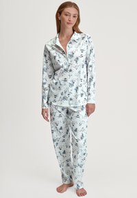 Lange mouwen pyjama set in lichtblauwe stof met een speels patroon van dieren en voorwerpen. Geknoopte shirt en rechte pijpen.
