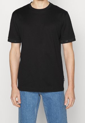 Schwarzes Baumwoll-T-Shirt mit rundem Ausschnitt, kurzen Ärmeln mit strukturiertem schwarzem Besatz und kleinem Logodetail am Ärmel.