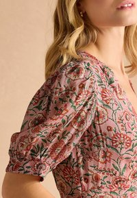 Blumenmusterkleid mit puffierten kurzen Ärmeln, mit einem pastellrosa Hintergrund und aufwendigen roten und grünen Stickereidetails.