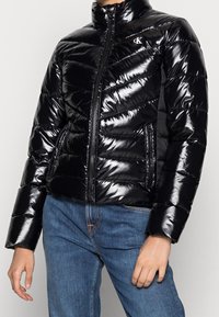 Czarna kurtka puchowa o błyszczącej powierzchni, skośnym wzorze pikowania, wysokim kołnierzu i zapinana na zamek. Posiada kieszenie boczne oraz akcent w postaci logo.