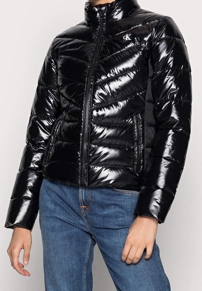 Czarna kurtka puchowa o błyszczącej powierzchni, skośnym wzorze pikowania, wysokim kołnierzu i zapinana na zamek. Posiada kieszenie boczne oraz akcent w postaci logo.