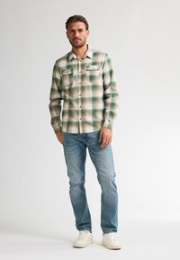 Geruite flanellen blouse in blauw, groen en wit met zakken met knopen, gecombineerd met lichtblauwe spijkerbroek en witte sneakers. Eenvoudig kraagontwerp.