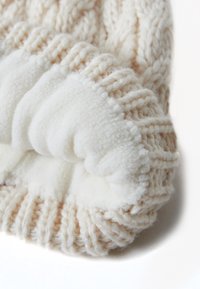Coperta lavorata a maglia in tonalità beige e crema con un morbido e soffice sotto bianco; presenta un design a coste che aumenta il calore e il comfort.
