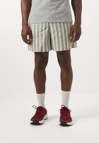 Striped swim shorts in olive green and white, with a loose fit. Paired with red athletic shoes and white crew socks.