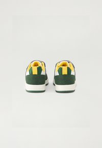 Λευκά και πράσινα αθλητικά παπούτσια με υφή από σουέτ στο πίσω μέρος, κίτρινες λεπτομέρειες και μινιμαλιστικό σχέδιο με χαμηλό προφίλ.