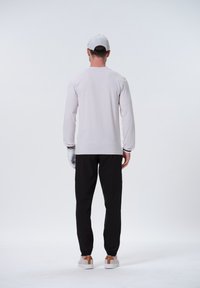 Langærmet lys grå skjorte med sorte detaljer, parret med sorte bukser og hvide sneakers med en brun hældetalje. Hvid kasket på hovedet.
