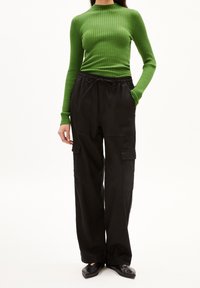 Vihreä ribbineulottu pitkähiha-paita ja mustat leveälahkeiset cargo-housut taskuilla. Mustat matalat kengät täydentävät asun. Yksinkertainen ja toimiva muotoilu.