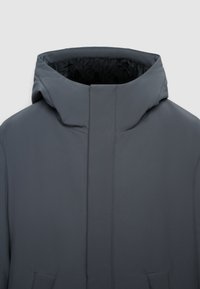 Giacca grigia con cappuccio, colletto alto, texture liscia, zip frontale nascosta e due tasche laterali. Fodera interna di colore nero.