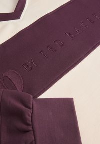 Paarse sweatshirt met een crèmekleurig paneel, met een geborduurd "BY TED BAKER" logo. V-hals ontwerp en gestructureerde mouwen.