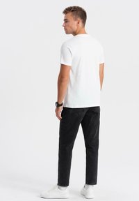 Vit t-shirt med kort ärm som är kombinerad med svarta jeans. T-shirten har en klassisk passform och jeansen har en vanlig passform med bakfickor.