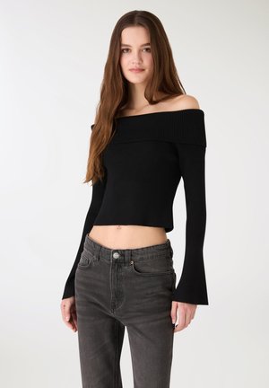 Czarny prążkowany krótki top z odkrytymi ramionami i długimi, rozkloszowanymi rękawami, w połączeniu z ciemnoszarymi, wysokim stanem jeansami z subtelnie zaznaczonymi guzikami.
