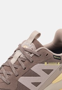 Svijetlosmeđi mokasini od suede-a i mrežaste tkanine imaju tonirane vezice, podstavljeni ovratnik, žute šavove i GORE-TEX logo sa strane.