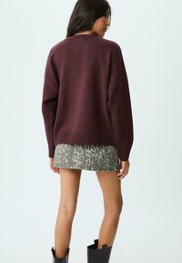Bordowy, oversize sweter z prążkowanym wykończeniem na rękawach i u dołu, zestawiony z szaro-leopardowym spódnicą, noszony z czarnymi, sięgającymi kolan kozaki.