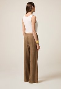 Bruna randiga vida byxor med en avslappnad passform, kombinerat med en vit ärmlös topp. Noterbart gult handledsaccessoar.