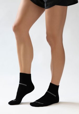 Schwarze Knöchelsocken mit einem gerippten Bündchen und einem dünnen weißen Streifen in der Mitte. Weicher Stoff, enganliegendes Design. Eignet sich für die Freizeit.