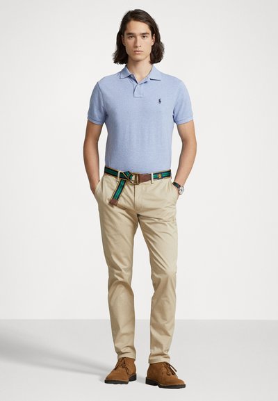 Polo de culoare albastră deschisă cu guler, chinos kaki, curea colorată cu dungi și pantofi din suede măsline. Design simplu și croială ajustată.