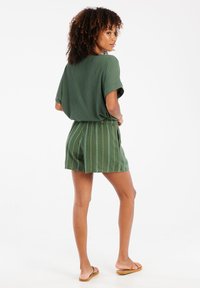 Haut vert à côtes avec une coupe décontractée, associé à un short vert à motifs présentant des rayures blanches verticales et une bordure. Porté avec des sandales marron.