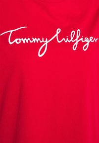 Rød bomulds t-shirt med hvid kursiv tekst "Tommy Hilfiger" hen over brystet. Enkel design med rund halsudskæring.