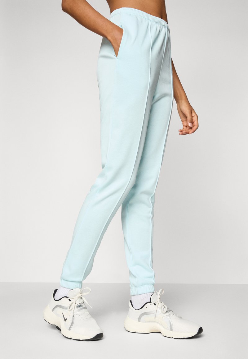Pantalones de chándal de color azul claro con corte ajustado, cinturilla elástica, bolsillos laterales y puños de canalé. Llevados con zapatillas deportivas blancas.