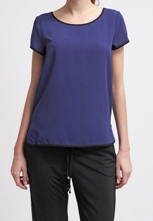 Top corto morado de manga corta con cuello redondo y ribete negro. Textura suave, corte relajado. Combinado con pantalones negros con cordón ajustable.