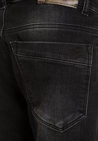 Černé džíny z denimu se zeslabeným povrchem. Obsahují jednu zadní kapsu s embosovaným logem a viditelnými švy.