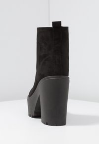 Mustat suede nilkkurit korkealla lohkarepohjalla, joissa on pehmeä pinta ja vetotappi takana. Pohjassa on uritettu kuvio.