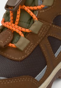 Bruna vandringsskor med texturerad tyg, orange snören och gröna accenter. Har en vadderad krage och gummisula för bra grepp.