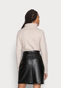 Beige coltrui met geribbelde textuur, gecombineerd met een zwarte leren minirok met een hoge taille en zijzakken.