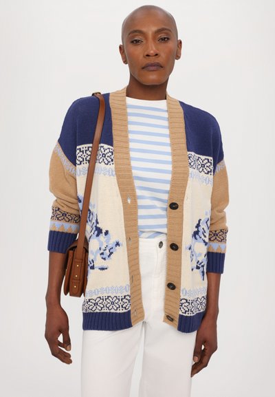 Strickjacke in einer Farbpalette aus Creme, Blau und Braun mit floralen Mustern, gerippten Bündchen und Knöpfen auf der Vorderseite. Darunter ein gestreiftes weißes Shirt.