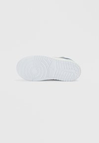 Λευκή σόλα αθλητικού παπουτσιού με σχεδιασμένη πρόσφυση, διαθέτει κυκλικά και γραμμικά αυλάκια, λεία επιφάνεια και ένα ελαφρώς ανυψωμένο λογότυπο.